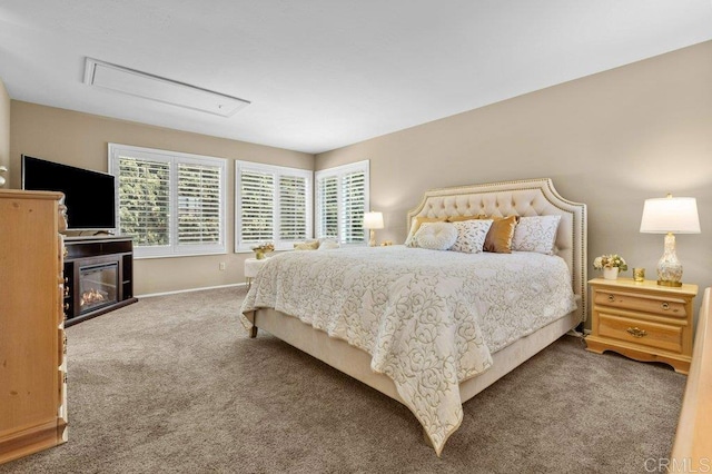 carpeted bedroom featuring baseboards, attic access, and a glass covered fireplace