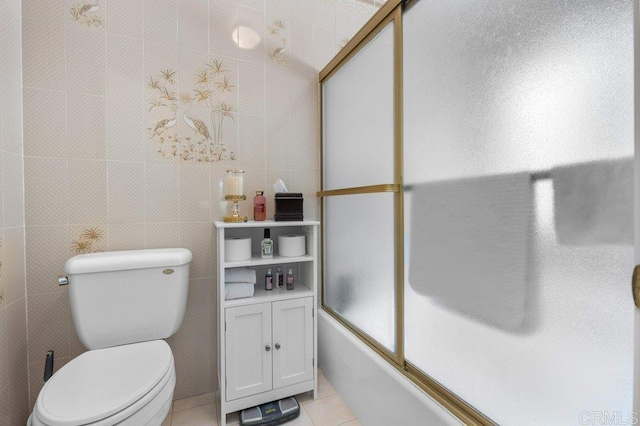 bathroom with tile walls, tile patterned flooring, bath / shower combo with glass door, and toilet