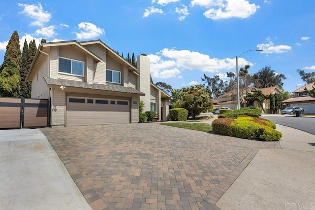 view of front of home with decorative driveway, an attached garage, a chimney, and a gate