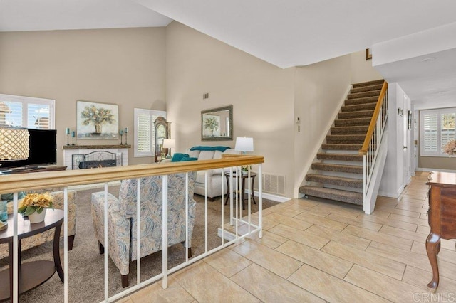 staircase with high vaulted ceiling, baseboards, a fireplace, and visible vents