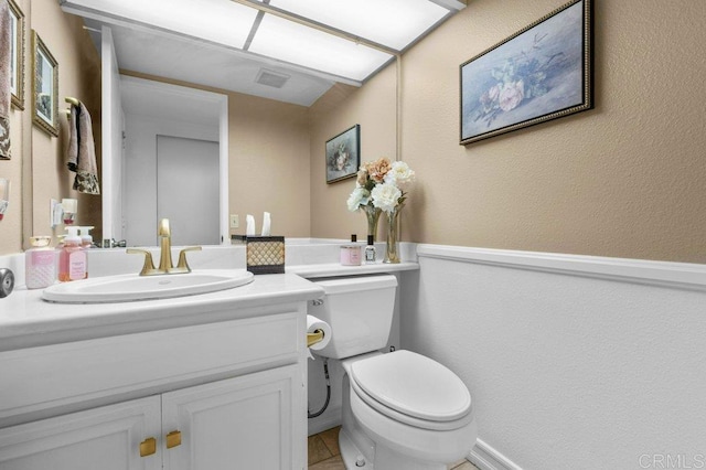 half bath featuring vanity, a textured wall, visible vents, and toilet