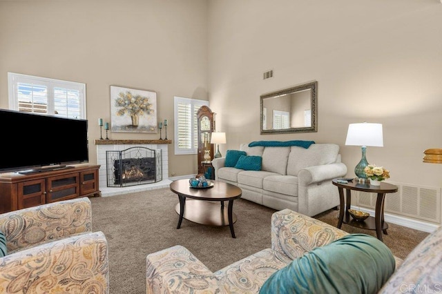 carpeted living area featuring a lit fireplace, a high ceiling, visible vents, and baseboards