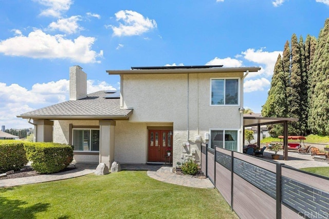 rear view of house featuring roof mounted solar panels, stucco siding, a yard, and a chimney