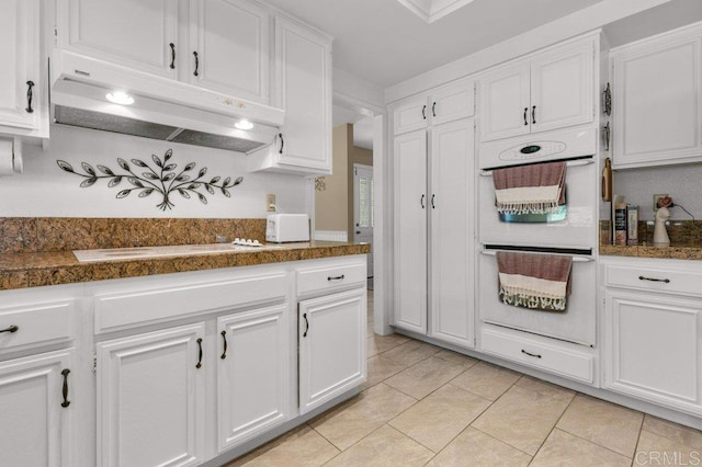 kitchen with dark countertops, under cabinet range hood, white appliances, and white cabinetry