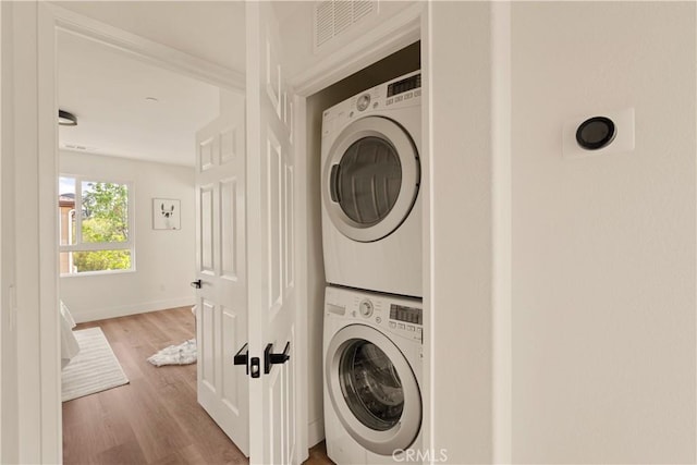 laundry area with laundry area, visible vents, wood finished floors, baseboards, and stacked washing maching and dryer