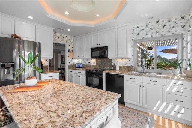 kitchen with a sink, a raised ceiling, black appliances, and white cabinetry