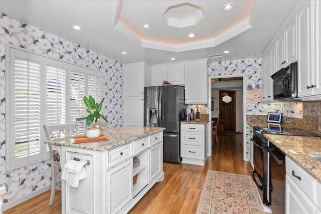 kitchen with a raised ceiling, white cabinets, black appliances, and light wood finished floors