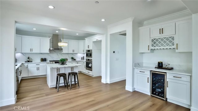 kitchen featuring wall chimney range hood, white cabinets, light wood finished floors, wine cooler, and ornamental molding