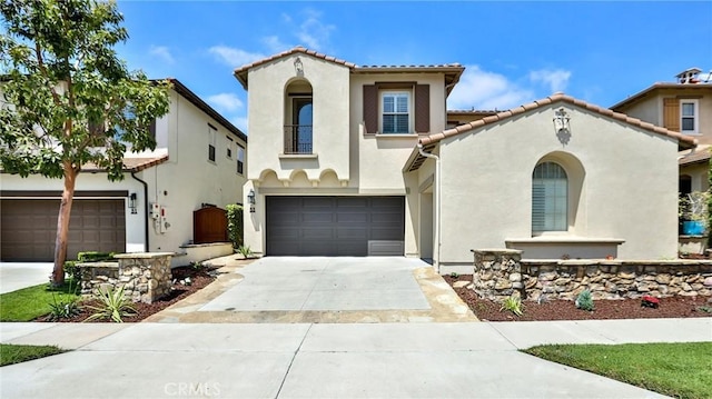 mediterranean / spanish house featuring an attached garage, stucco siding, a tiled roof, and concrete driveway