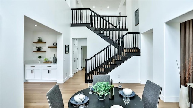 dining room with light wood-type flooring, stairs, a towering ceiling, and baseboards