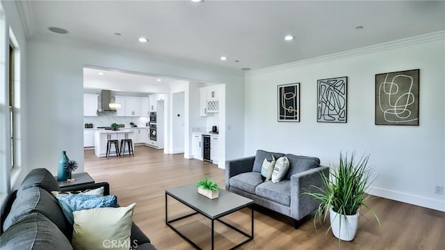 living area featuring wine cooler, baseboards, crown molding, and light wood-style flooring