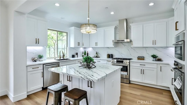 kitchen with white cabinets, appliances with stainless steel finishes, a sink, wall chimney exhaust hood, and a center island