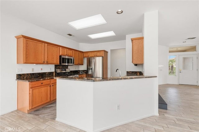 37388 Medjool, Palm Desert, CA 92211 - kitchen with stainless steel appliances, dark stone counters, light wood-type flooring, a peninsula, and brown cabinetry