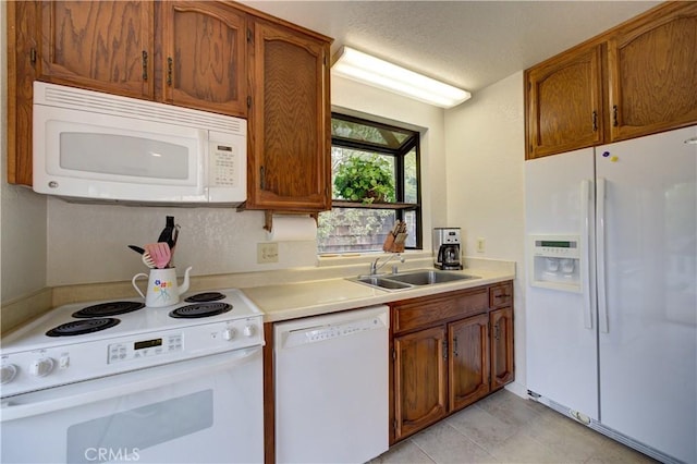 kitchen with brown cabinetry, a sink, light countertops, light tile patterned floors, and white appliances