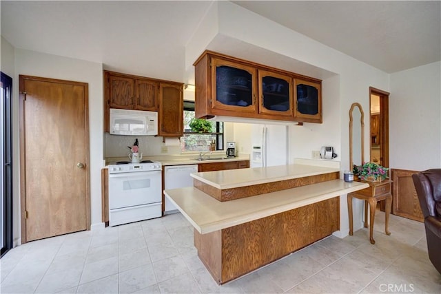 kitchen featuring light countertops, glass insert cabinets, a peninsula, and white appliances