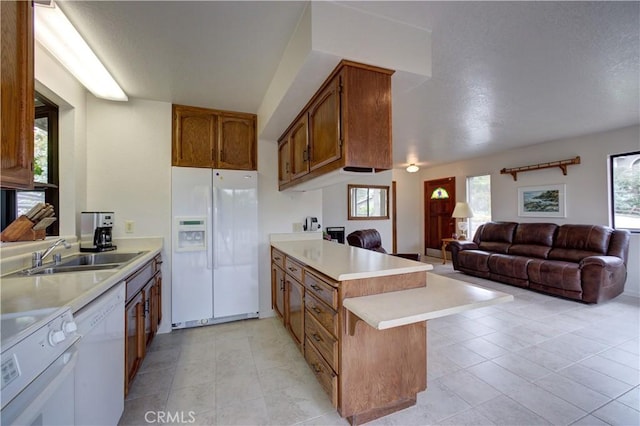 kitchen featuring brown cabinets, a sink, light countertops, a peninsula, and white appliances