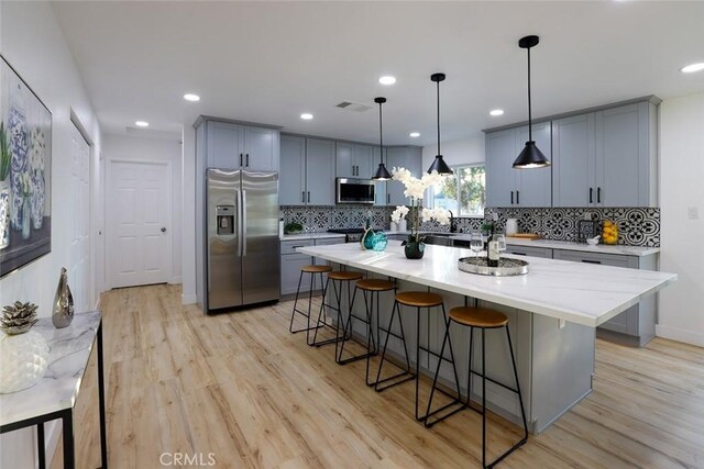 1402 E Luray St, Long Beach, CA 90807 - kitchen featuring a kitchen breakfast bar, backsplash, appliances with stainless steel finishes, gray cabinetry, and light wood-style floors