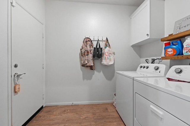 clothes washing area with baseboards, washing machine and dryer, light wood-type flooring, and cabinet space