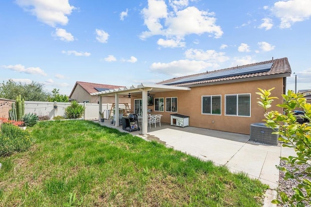 back of property with ceiling fan, stucco siding, roof mounted solar panels, a fenced backyard, and a lawn