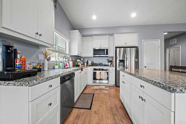 kitchen with visible vents, light wood-style floors, dark stone counters, a sink, and appliances with stainless steel finishes