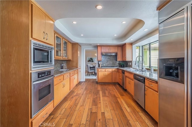 kitchen with wood-type flooring, built in appliances, recessed lighting, a tray ceiling, and a sink