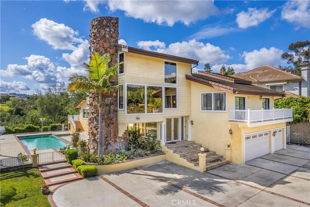 back of house featuring a balcony, an outdoor pool, stucco siding, a chimney, and driveway