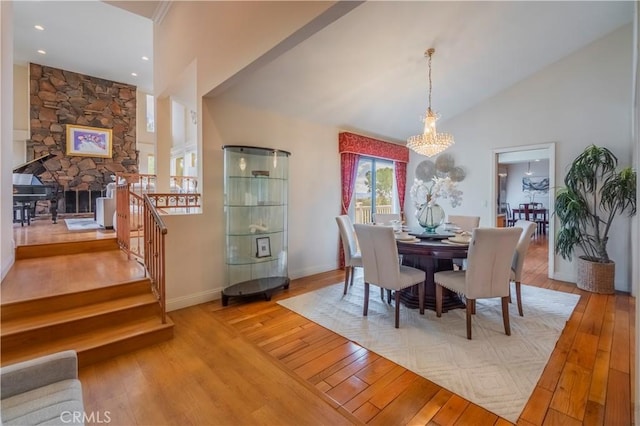 dining room featuring a stone fireplace, hardwood / wood-style flooring, stairway, baseboards, and a notable chandelier