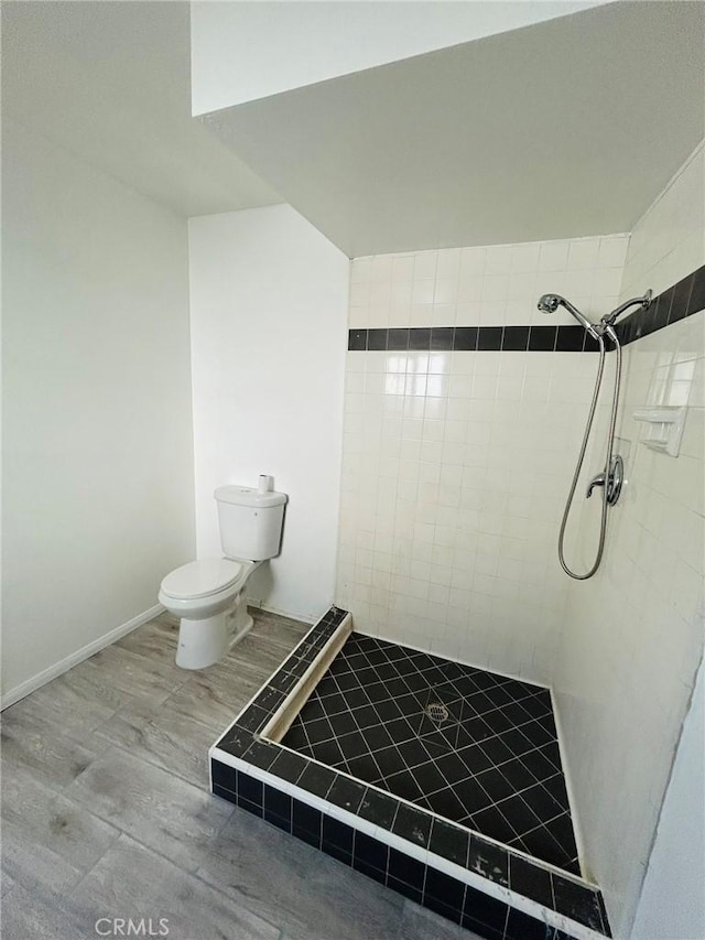 full bath featuring baseboards, a tile shower, toilet, and wood finished floors
