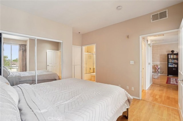 bedroom featuring light wood finished floors, baseboards, ensuite bathroom, visible vents, and a closet