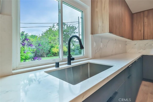 kitchen featuring brown cabinetry, decorative backsplash, modern cabinets, light stone counters, and a sink