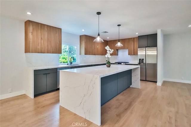 kitchen with appliances with stainless steel finishes, hanging light fixtures, a sink, light wood-style floors, and recessed lighting