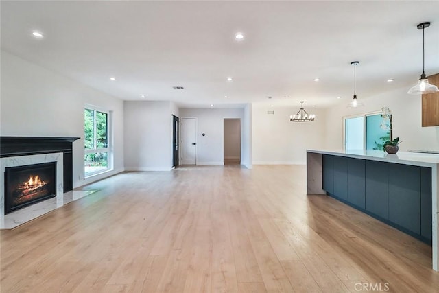 unfurnished living room featuring visible vents, recessed lighting, light wood-style flooring, a notable chandelier, and a premium fireplace