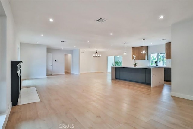 unfurnished living room with recessed lighting, baseboards, a sink, and light wood-style flooring