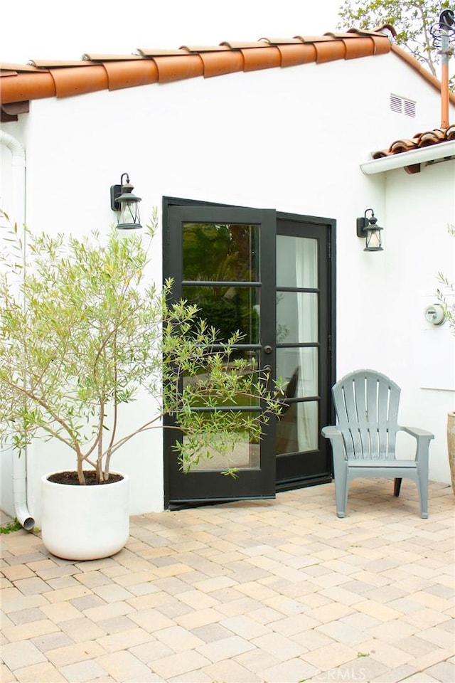property entrance with visible vents, a patio, stucco siding, and a tiled roof