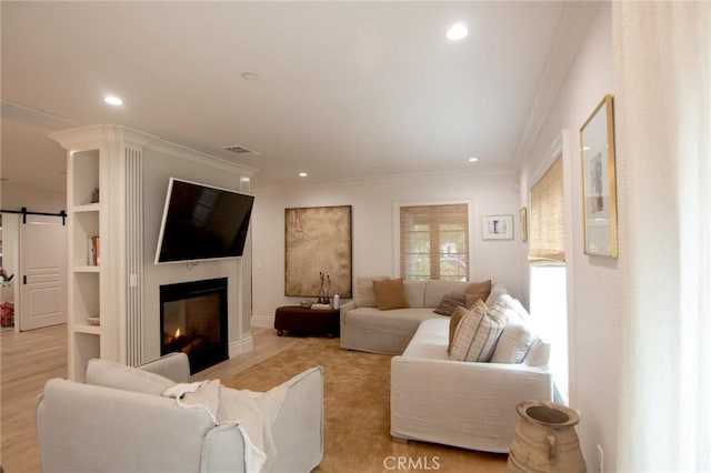 living room featuring a glass covered fireplace, ornamental molding, recessed lighting, and a barn door