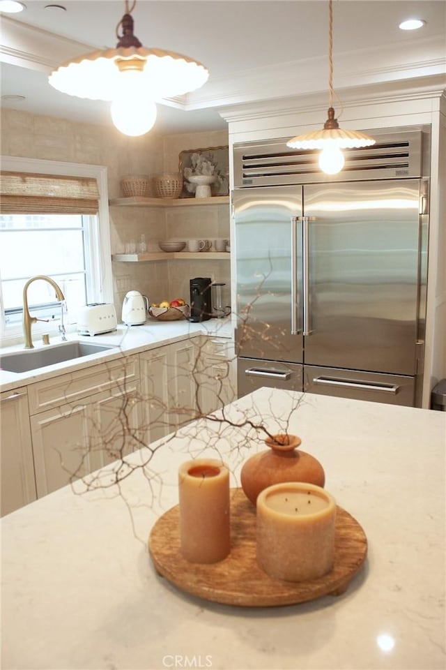 kitchen featuring open shelves, light stone countertops, a sink, ornamental molding, and stainless steel built in refrigerator