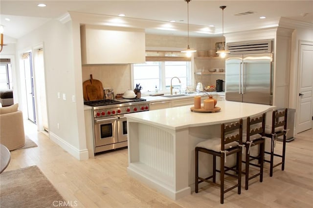 kitchen with a kitchen breakfast bar, high quality appliances, visible vents, a sink, and light wood-style floors