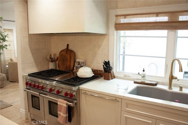kitchen featuring light wood-style floors, light countertops, a sink, backsplash, and double oven range
