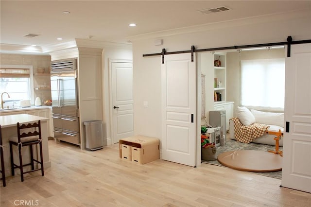 interior space with a sink, a barn door, ornamental molding, and light wood finished floors