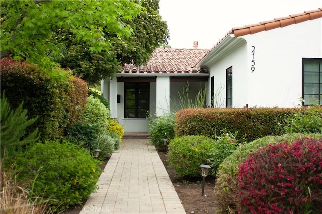property entrance with stucco siding, a tiled roof, and a chimney