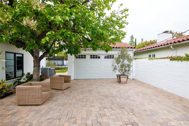 view of patio with a trampoline, central AC unit, a garage, fence, and an outdoor structure