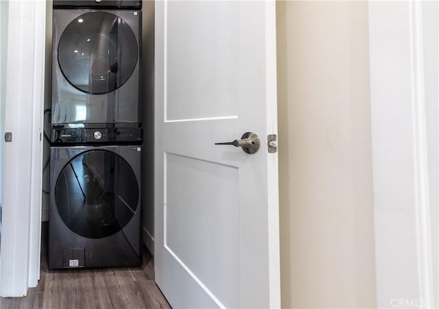 clothes washing area with stacked washer / drying machine, wood finished floors, and laundry area