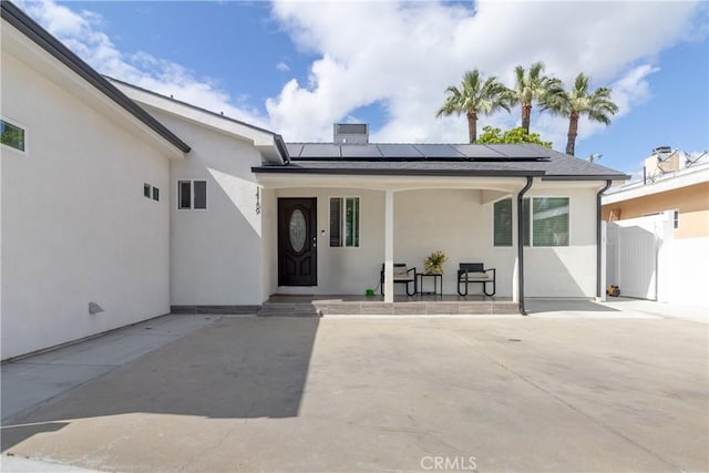 view of exterior entry with a gate, stucco siding, covered porch, and solar panels