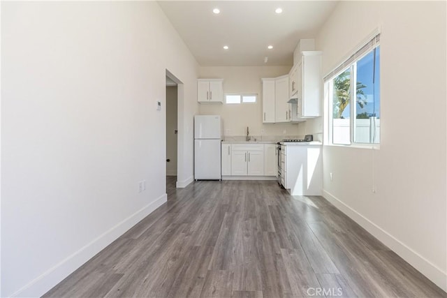 kitchen with baseboards, white appliances, wood finished floors, and white cabinetry