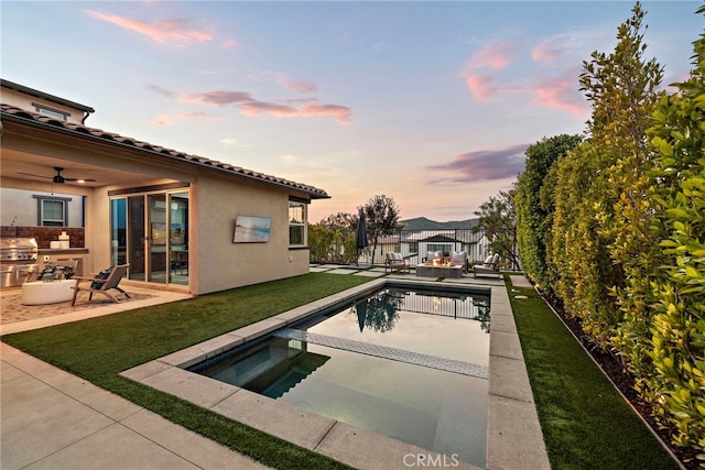 pool at dusk with a patio area, a yard, an in ground hot tub, and an outdoor kitchen