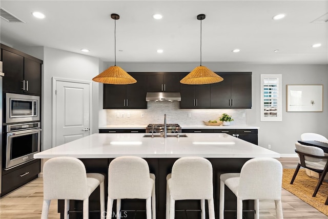 kitchen with appliances with stainless steel finishes, a breakfast bar, a sink, under cabinet range hood, and visible vents
