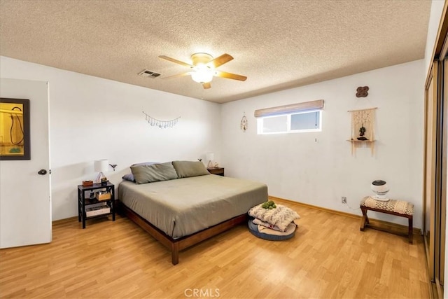 bedroom featuring ceiling fan, light wood finished floors, a textured ceiling, and visible vents