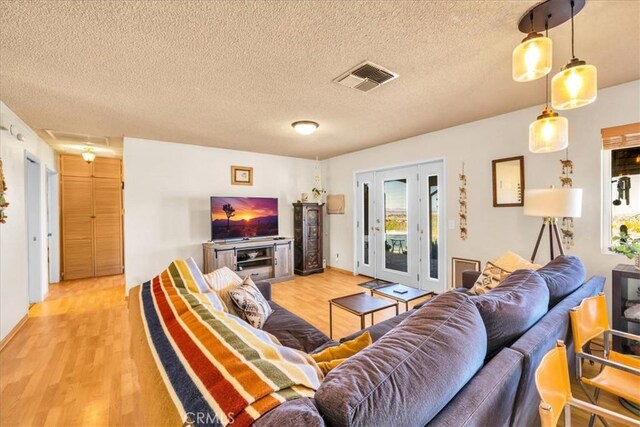 living room featuring light wood finished floors, a textured ceiling, french doors, baseboards, and visible vents