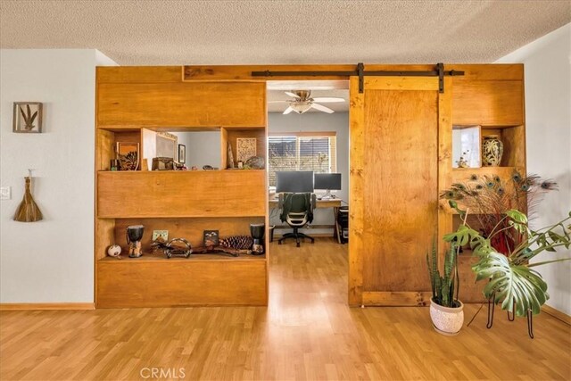 office area with wood finished floors, baseboards, a barn door, a textured ceiling, and a ceiling fan