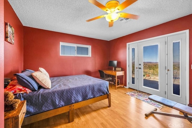 bedroom with a textured ceiling, access to exterior, a ceiling fan, wood finished floors, and visible vents